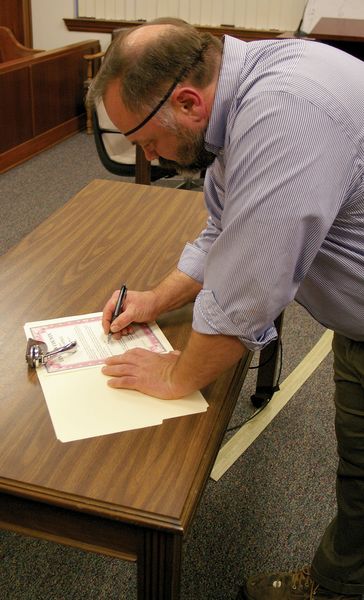 Tony Berget signs oath. Photo by Kootenai Valley Record.